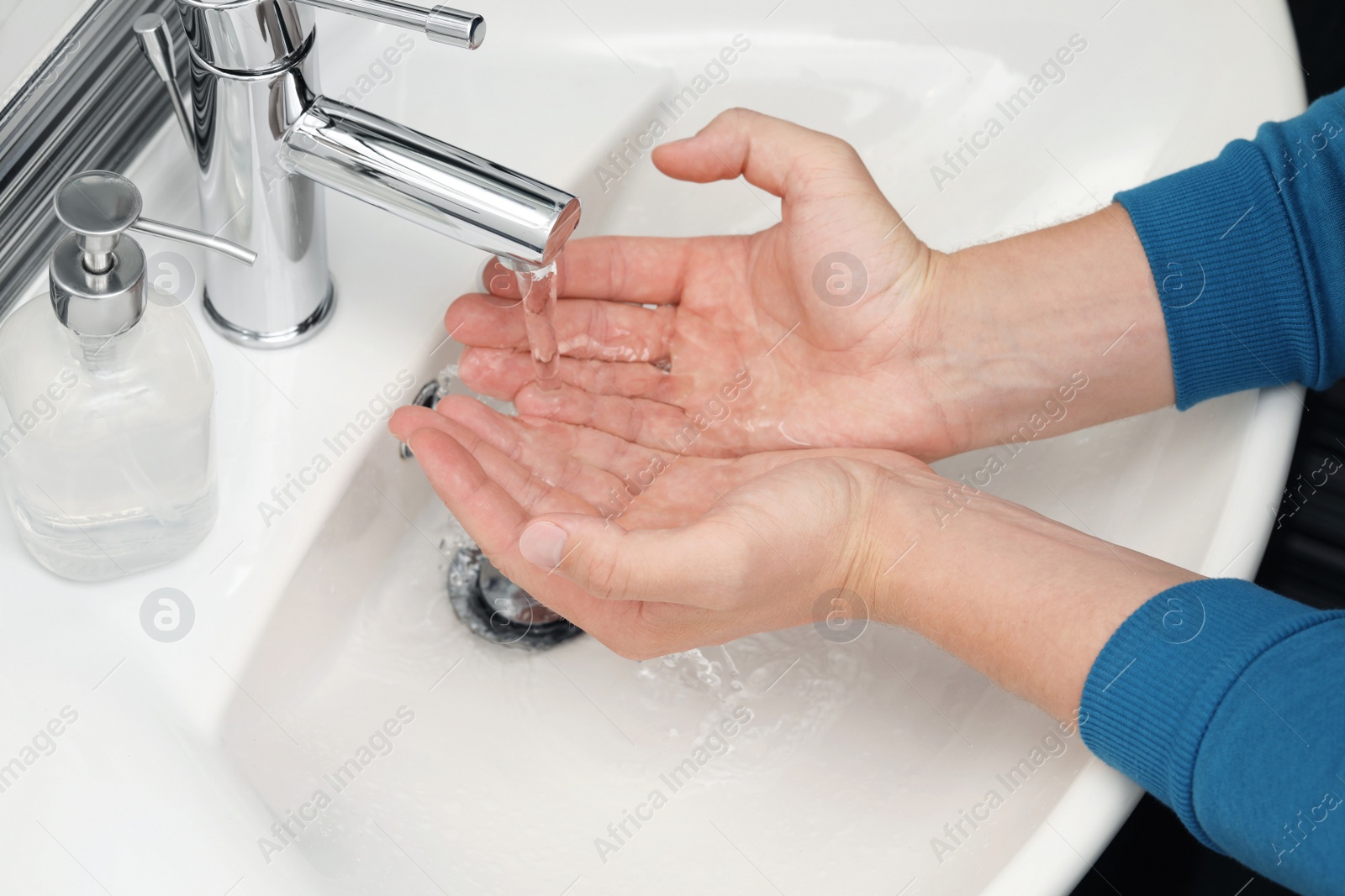 Photo of Man using water tap to wash hands in bathroom, closeup