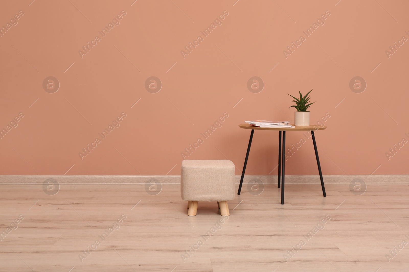 Photo of Comfortable ottoman and table near pale pink wall indoors, space for text