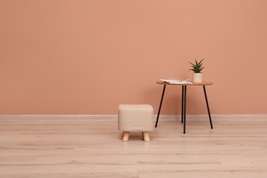 Photo of Comfortable ottoman and table near pale pink wall indoors, space for text