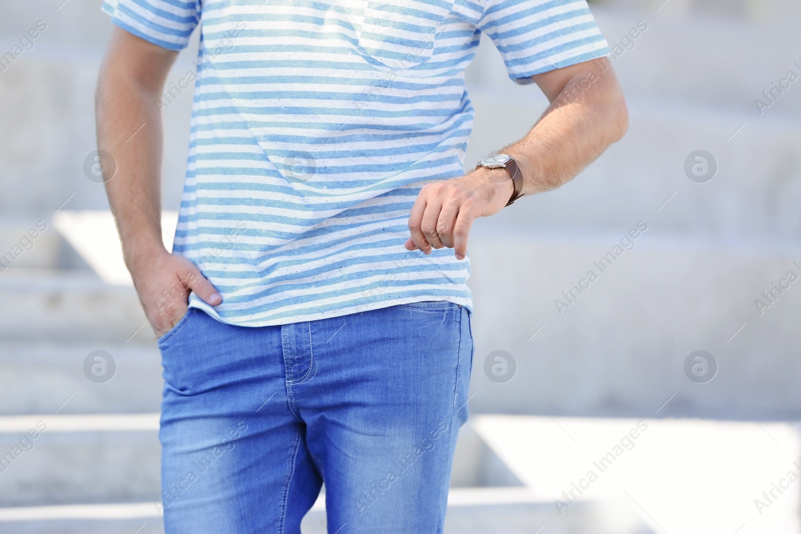 Photo of Young hipster man in stylish jeans standing near stairs outdoors