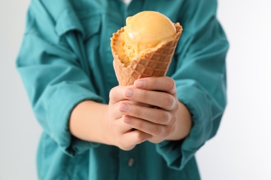 Woman holding yellow ice cream in wafer cone on light background, closeup