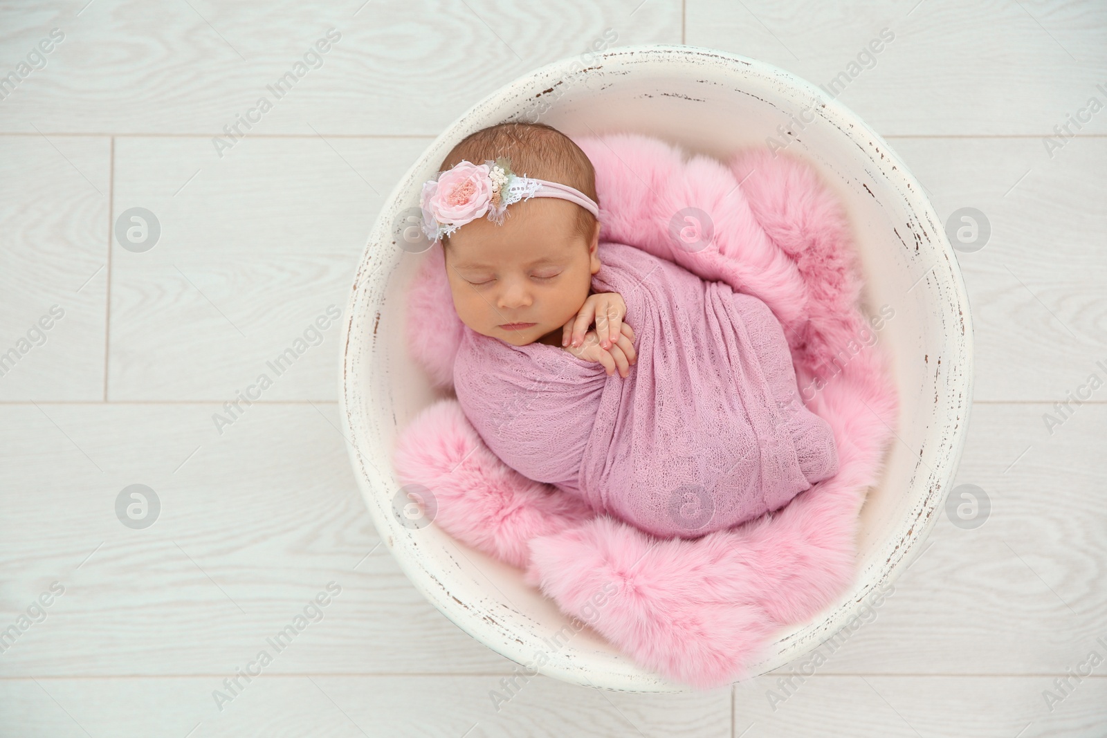 Photo of Adorable newborn girl lying in baby nest on light background, top view