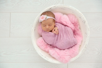 Photo of Adorable newborn girl lying in baby nest on light background, top view