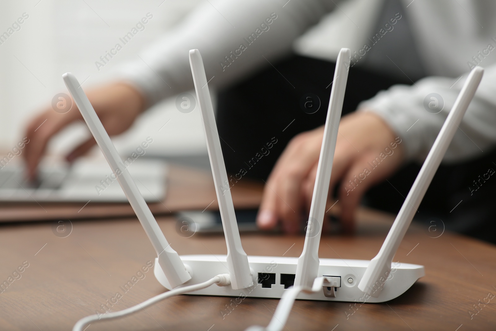 Photo of Man with laptop and smartphone working at wooden table, focus on Wi-Fi router