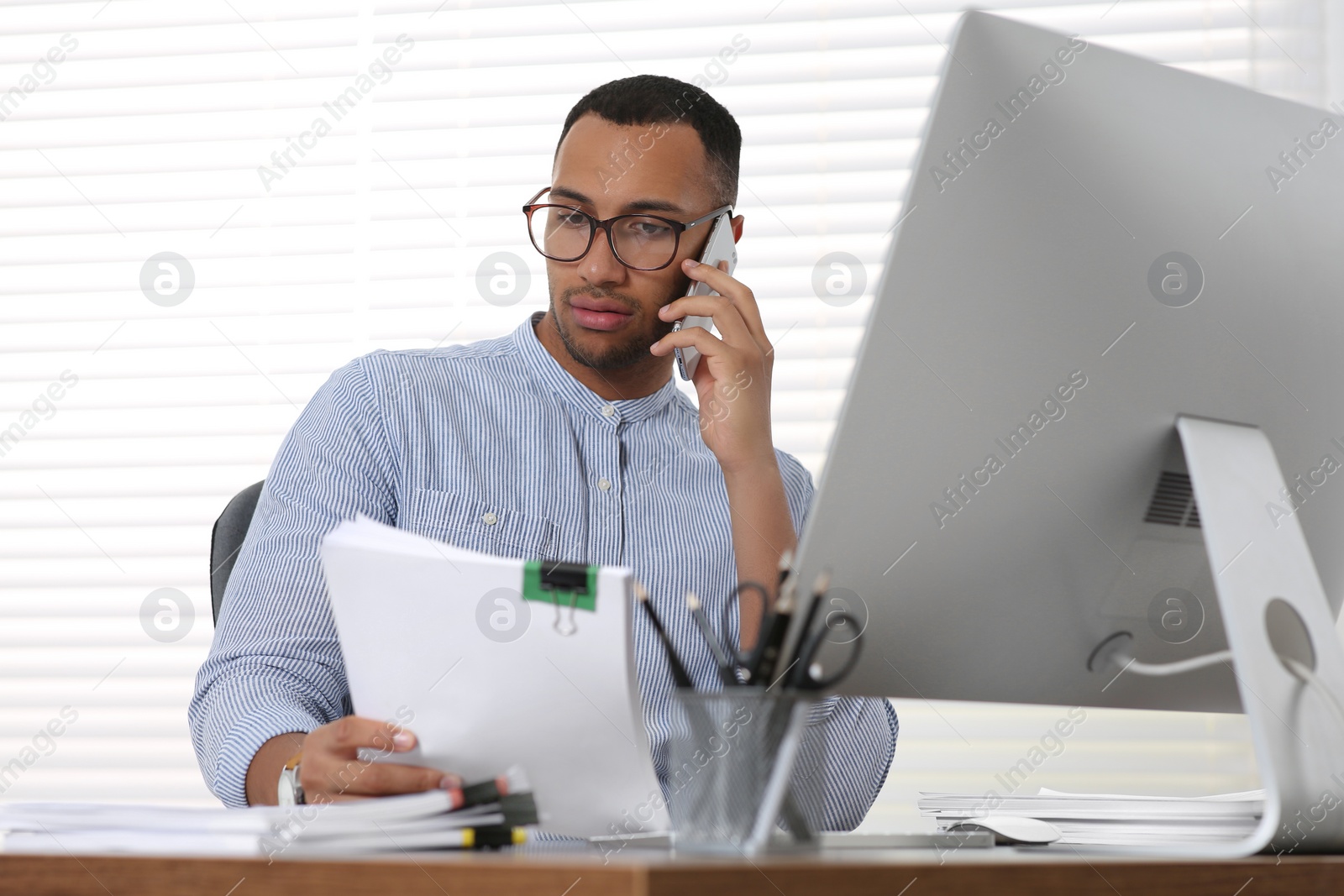 Photo of Man talking on phone while working with documents at wooden table in office