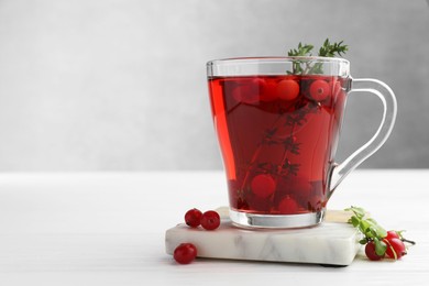 Photo of Tasty hot cranberry tea with thyme and fresh berries in glass cup on white wooden table