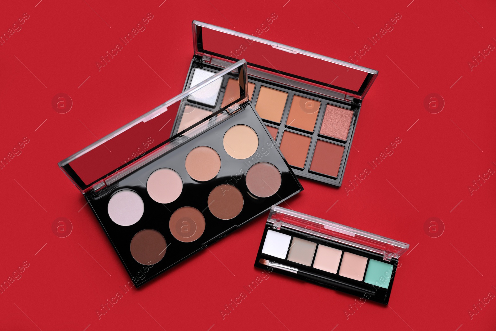 Photo of Colorful contouring palettes with brush on red background, flat lay. Professional cosmetic product