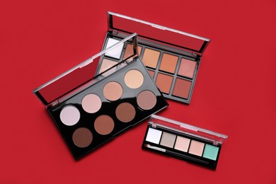Photo of Colorful contouring palettes with brush on red background, flat lay. Professional cosmetic product