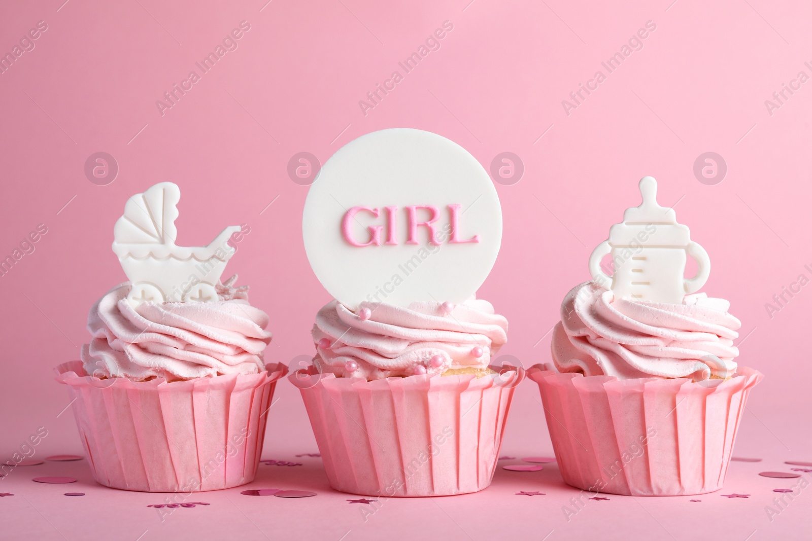 Photo of Beautifully decorated baby shower cupcakes for girl with cream and toppers on pink background