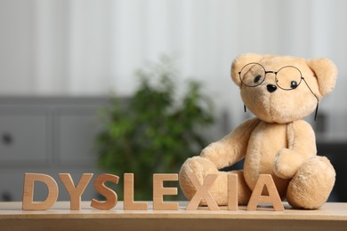 Photo of Teddy bear in glasses and word Dyslexia made of letters on wooden table indoors