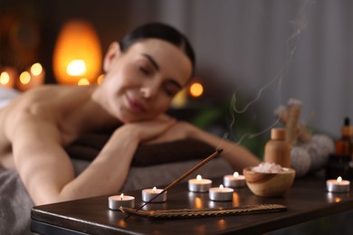Photo of Spa therapy. Beautiful young woman lying on massage table in salon, focus on burning candles, salt and incense stick