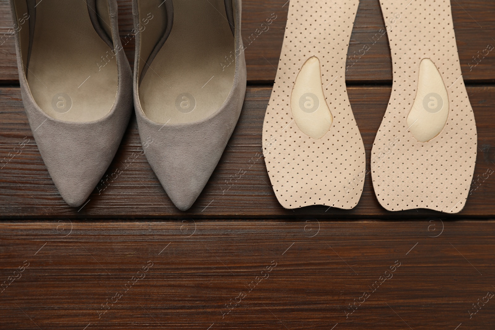 Photo of Orthopedic insoles near high heel shoes on floor, flat lay. Space for text