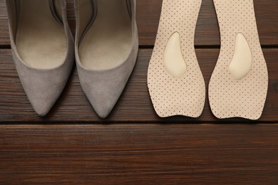 Photo of Orthopedic insoles near high heel shoes on floor, flat lay. Space for text