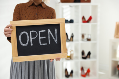 Photo of Female business owner holding OPEN sign in boutique, closeup. Space for text