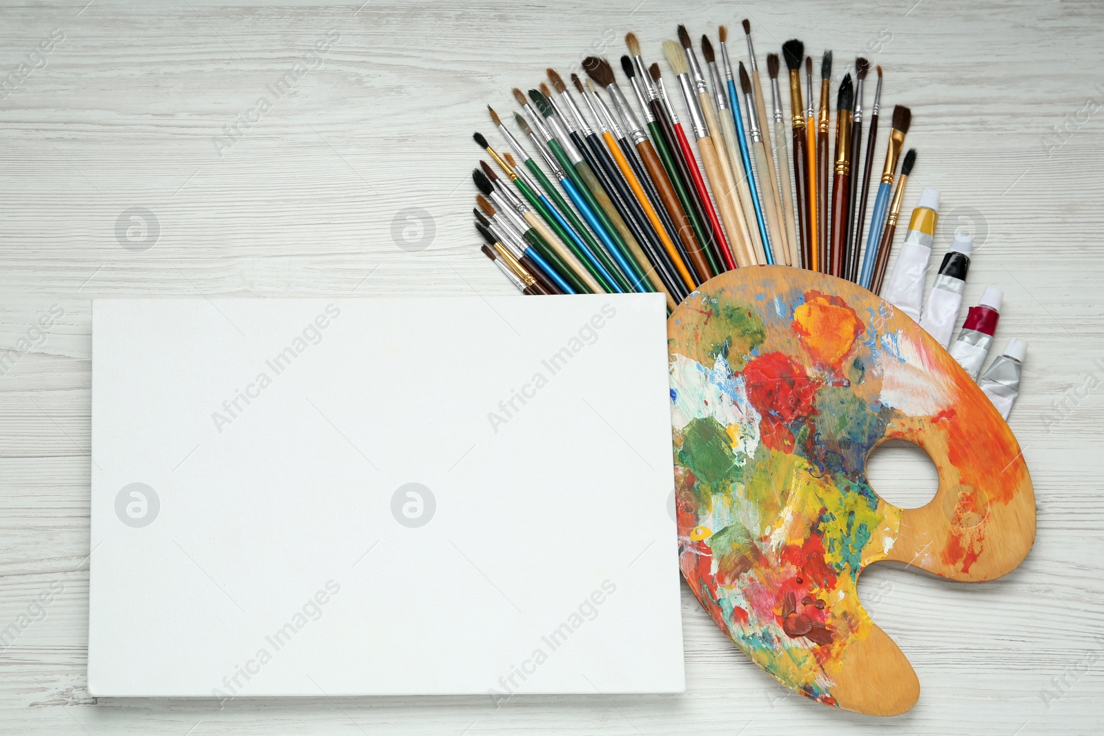 Photo of Blank canvas, brushes, palette and paints on white wooden table, flat lay. Space for text