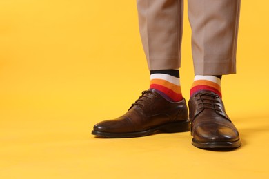 Photo of Man in stylish colorful socks, shoes and pants on yellow background, closeup. Space for text