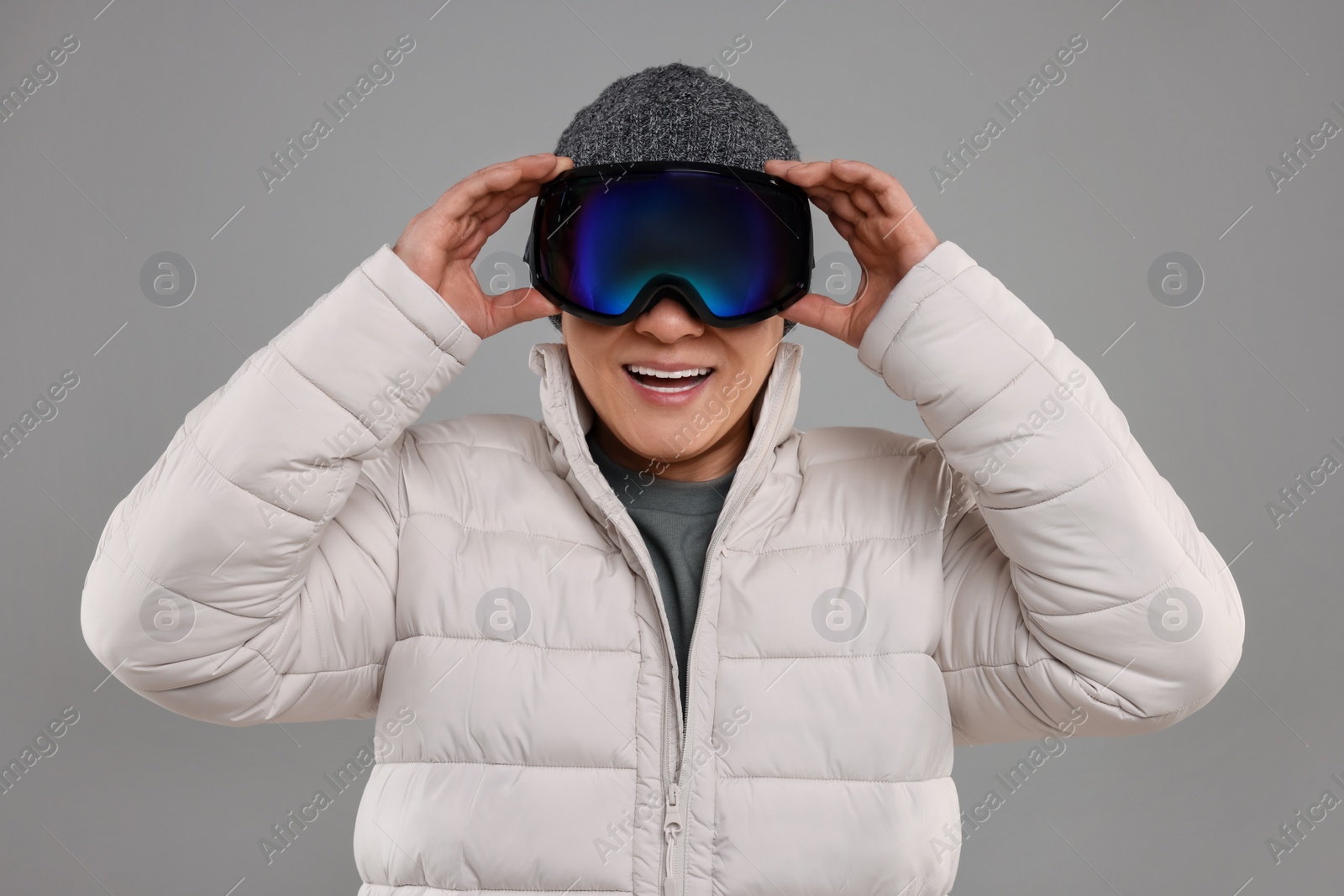 Photo of Winter sports. Happy man in ski goggles on grey background