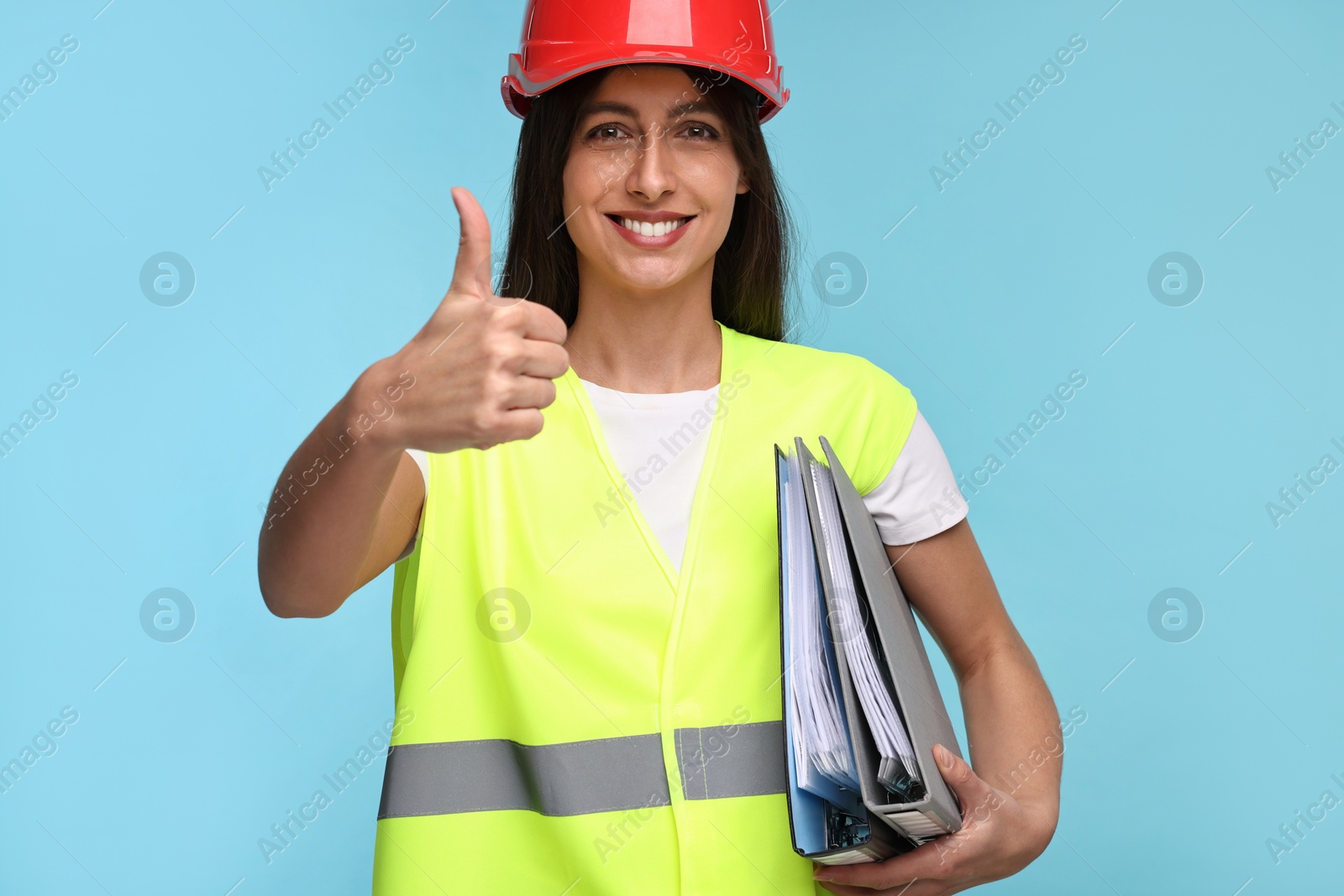 Photo of Architect in hard hat with folders showing thumbs up on light blue background