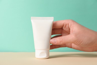 Photo of Tube of hand cream on beige table against turquoise background, closeup