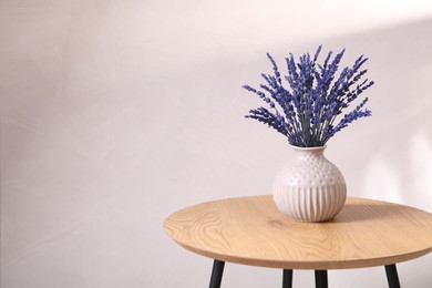 Photo of Bouquet of beautiful preserved lavender flowers on wooden table near beige wall, space for text