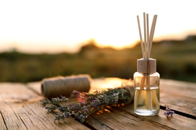 Photo of Reed air freshener and fresh lavender flowers on wooden table in field. Space for text