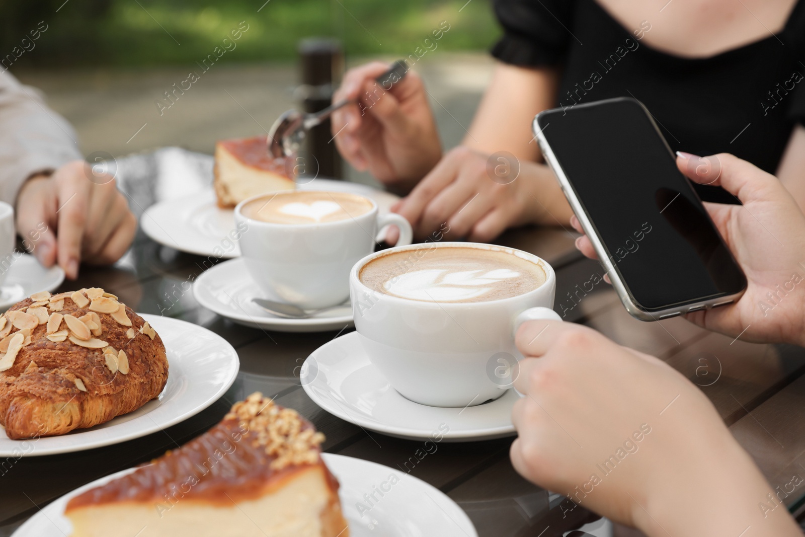 Photo of Friends drinking coffee at wooden table in outdoor cafe, closeup