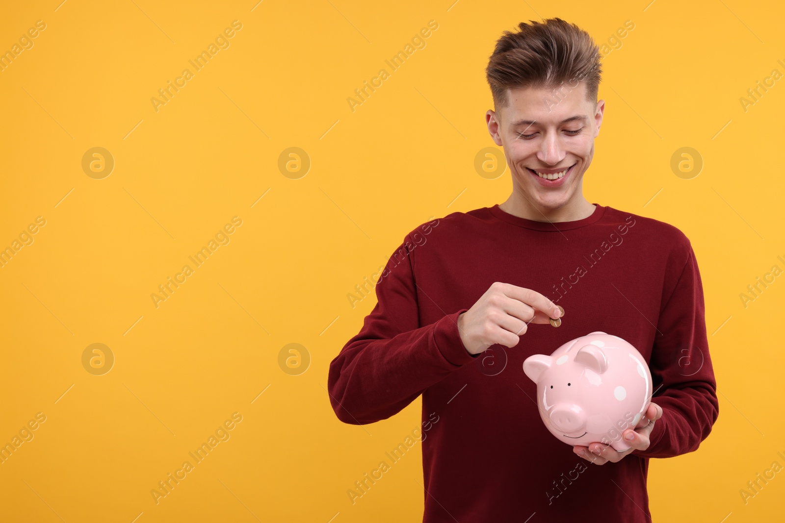 Photo of Happy man putting coin into piggy bank on yellow background. Space for text