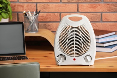 Photo of Modern electric fan heater near laptop and notebooks on wooden table in office