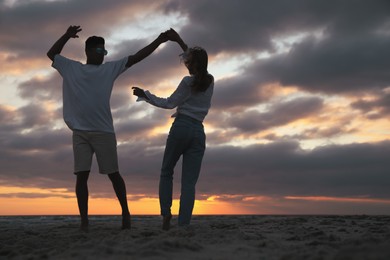 Happy couple dancing on beach at sunset