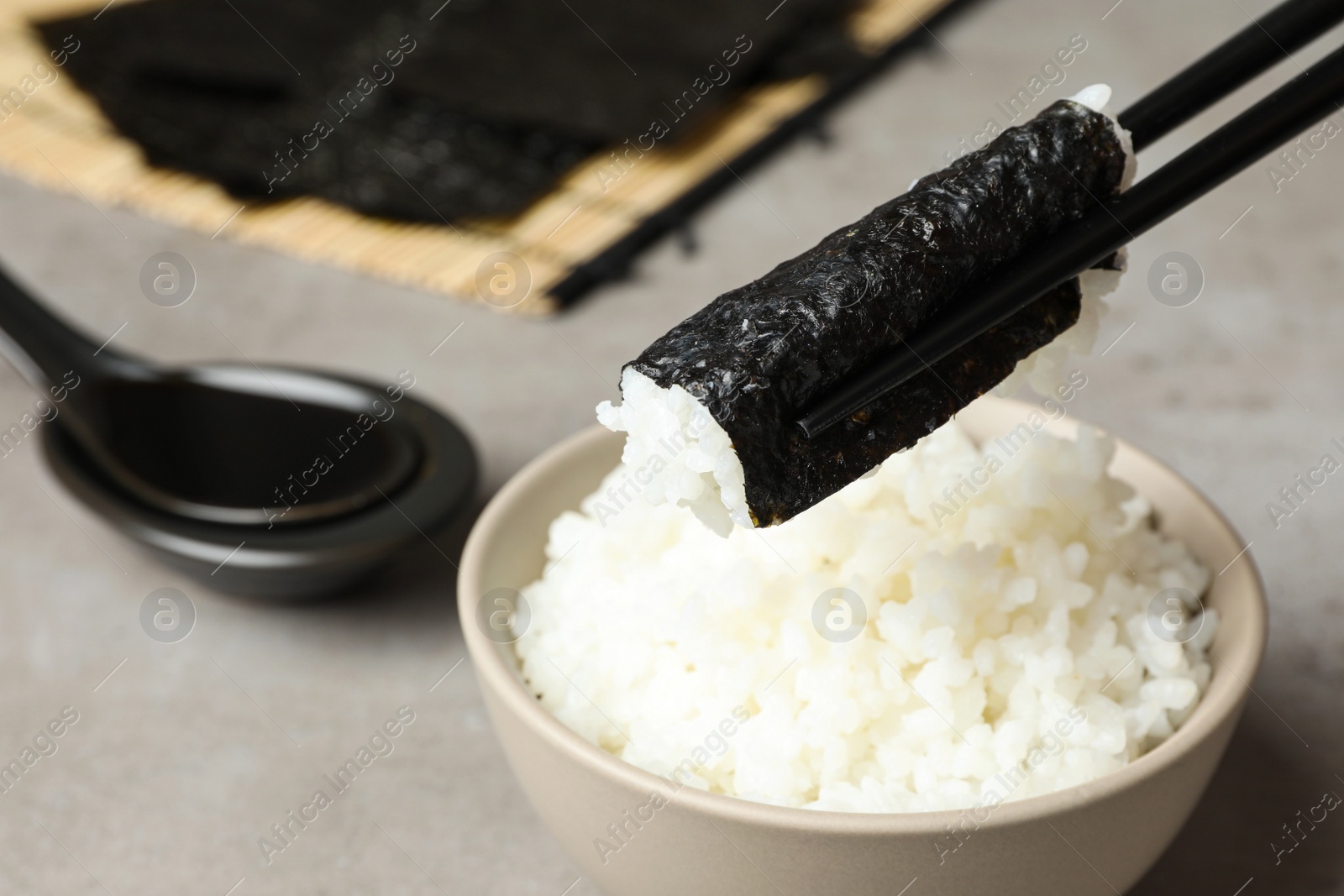 Photo of Holding nori with rice over grey table, closeup. Space for text