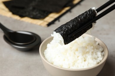 Photo of Holding nori with rice over grey table, closeup. Space for text