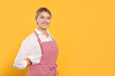 Photo of Beautiful young woman in clean striped apron on orange background. Space for text