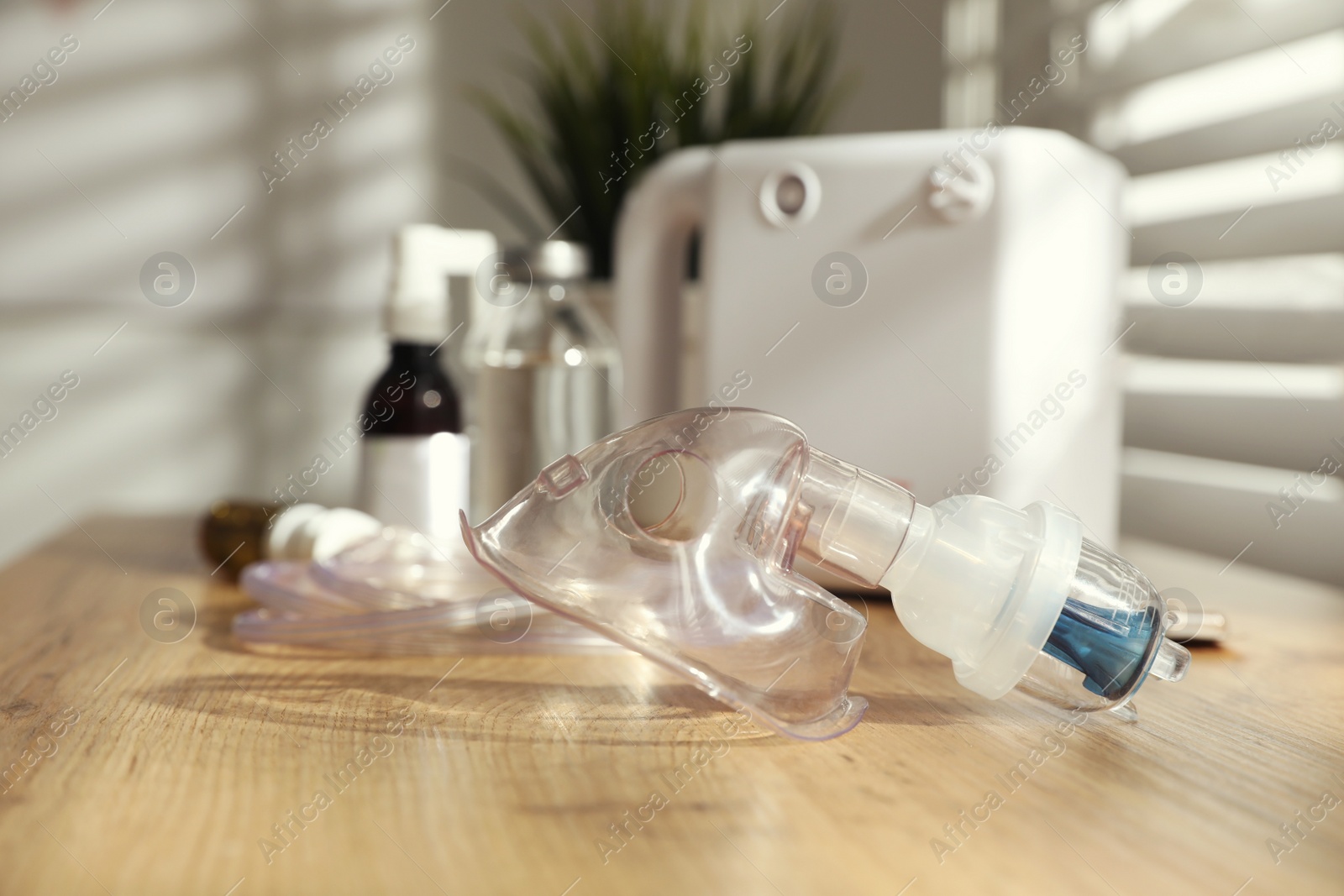 Photo of Face mask near nebulizer and medications on wooden table indoors. Inhalation equipment