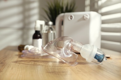 Photo of Face mask near nebulizer and medications on wooden table indoors. Inhalation equipment