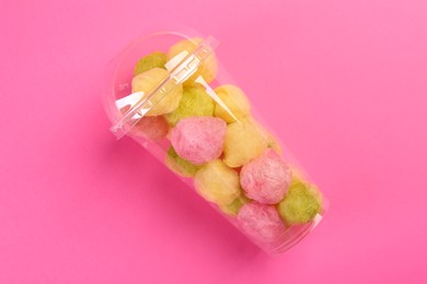 Photo of Plastic cup with color cotton balls on pink background, top view. Sweet candy