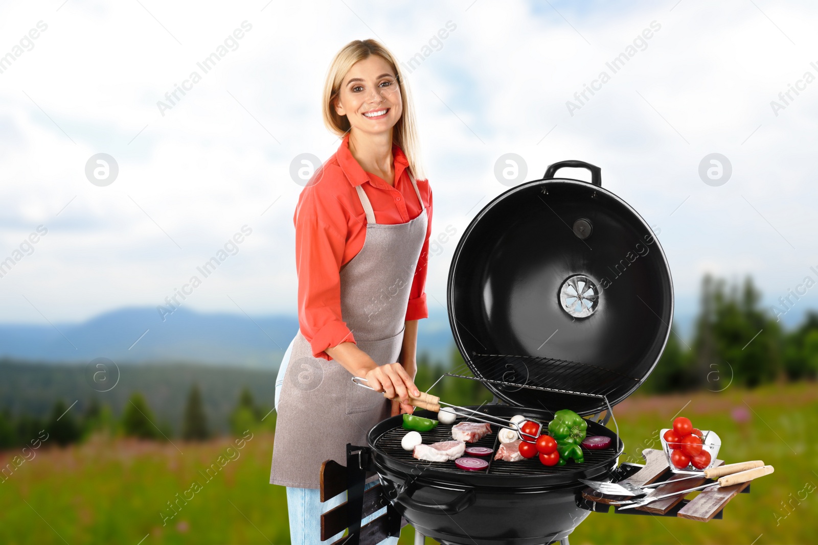 Image of Woman in apron cooking on barbecue grill in park. Picnic time