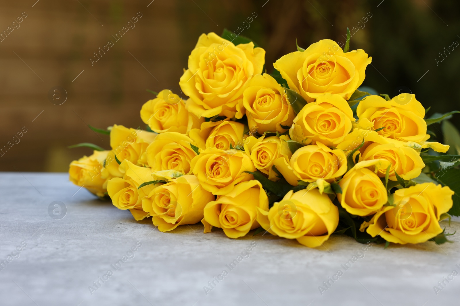 Photo of Beautiful bouquet of yellow roses on light table outdoors