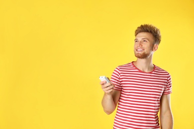 Young man with air conditioner remote on yellow background. Space for text