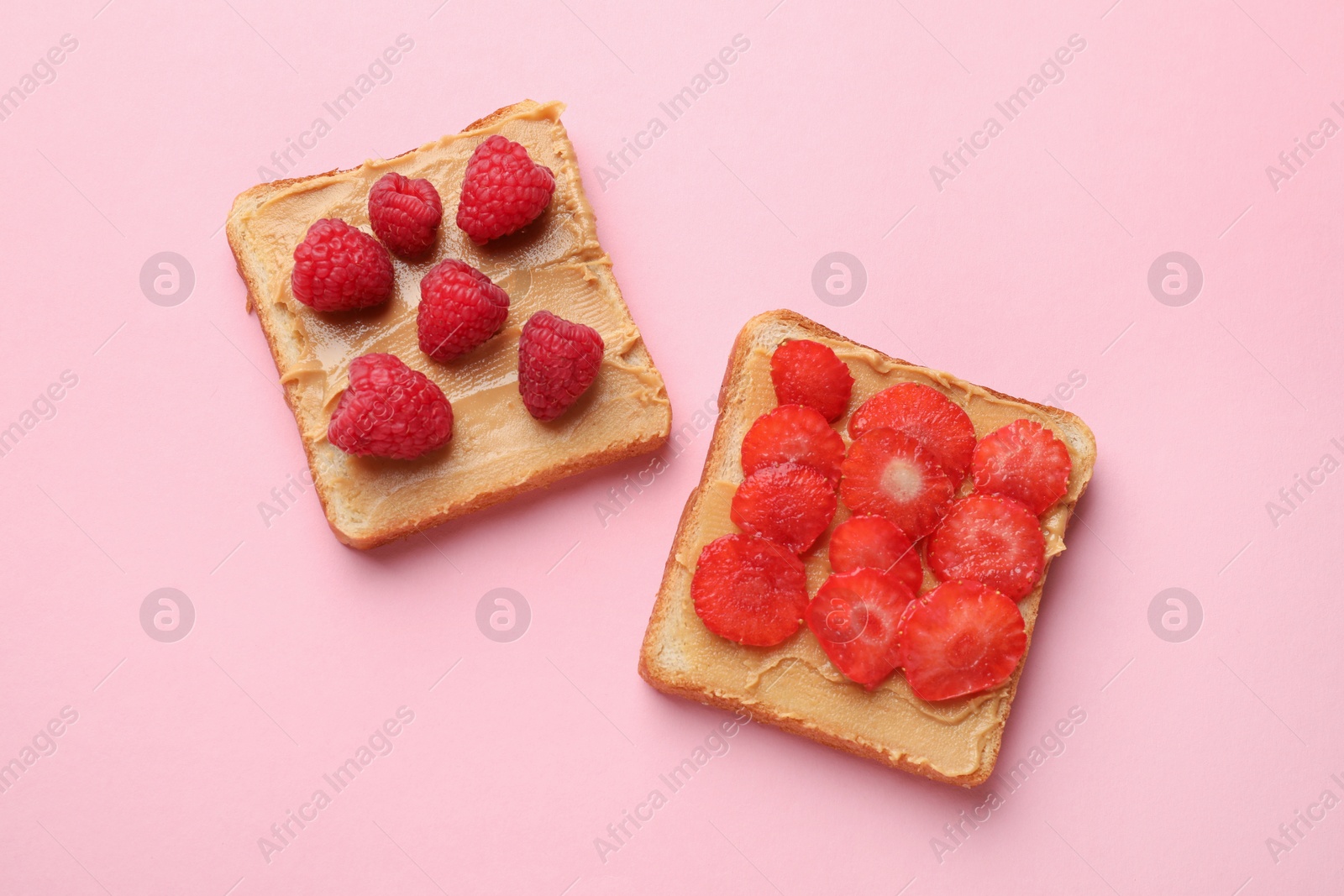 Photo of Tasty peanut butter sandwiches with fresh berries on pink background, flat lay