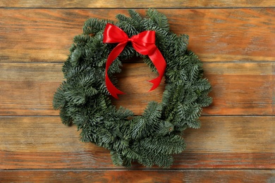 Photo of Christmas wreath made of fir tree branches with red ribbon on wooden background