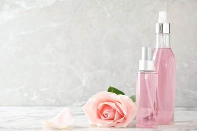 Photo of Bottles of essential oil and rose on marble table. Space for text