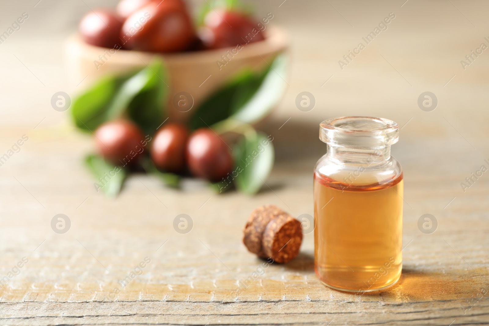 Photo of Glass bottle with jojoba oil on wooden table. Space for text