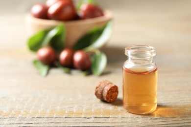 Photo of Glass bottle with jojoba oil on wooden table. Space for text