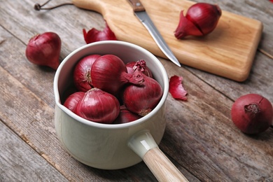 Photo of Saucepan with ripe red onions on wooden table