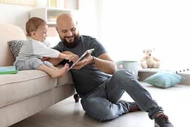 Photo of Dad reading book with his little son in living room