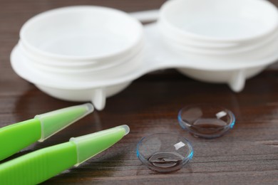 Contact lenses, tweezers and case on wooden table, closeup