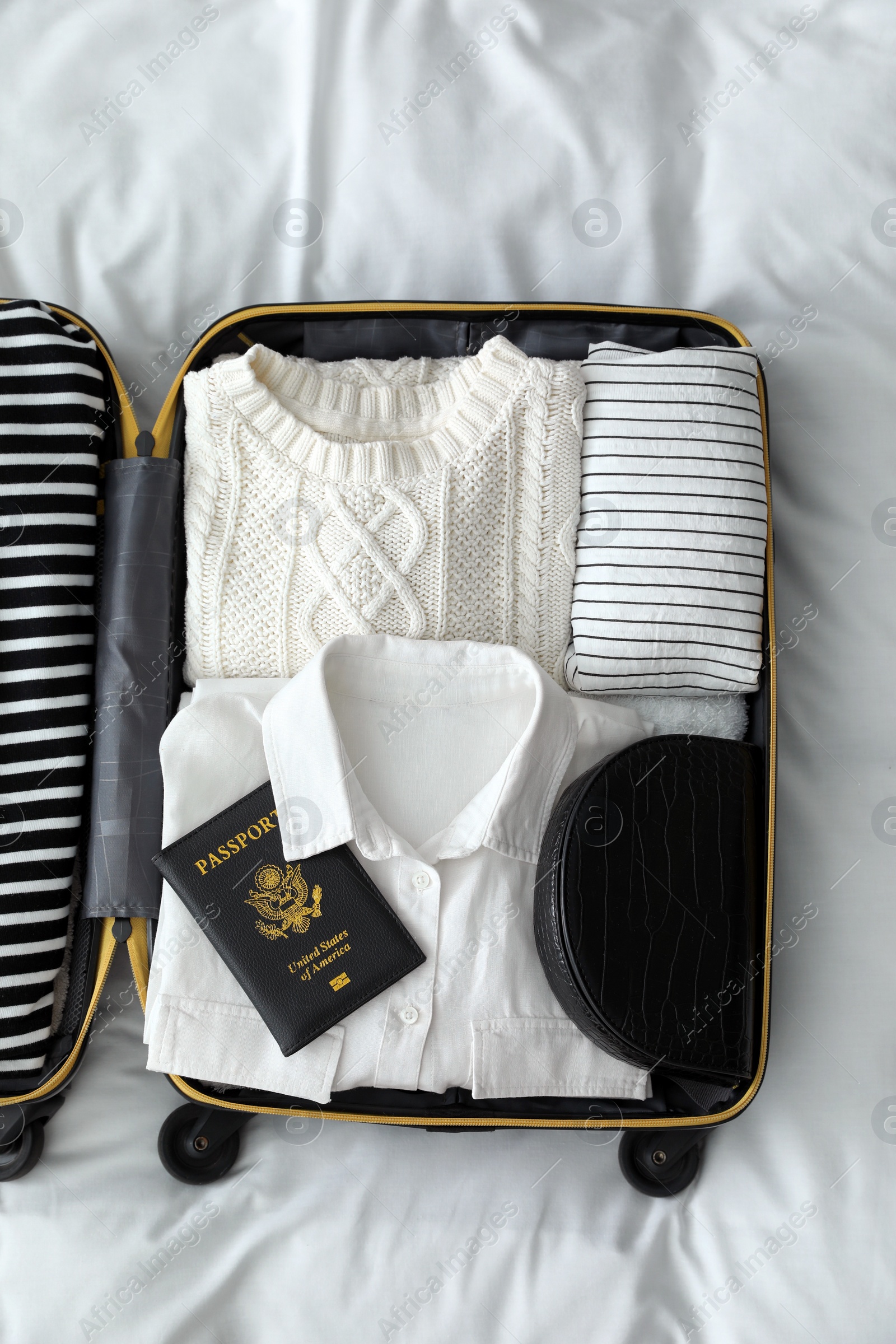 Photo of Open suitcase with clothes, passport and bag on bed, top view