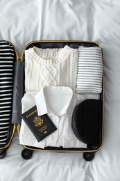 Open suitcase with clothes, passport and bag on bed, top view