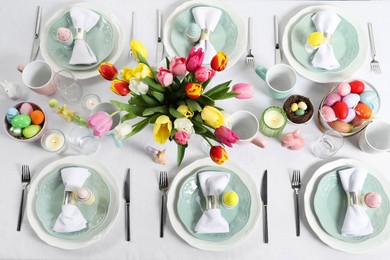Easter celebration. Festive table setting with beautiful flowers and painted eggs, flat lay