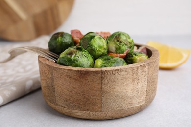 Delicious roasted Brussels sprouts and bacon in bowl on light table, closeup